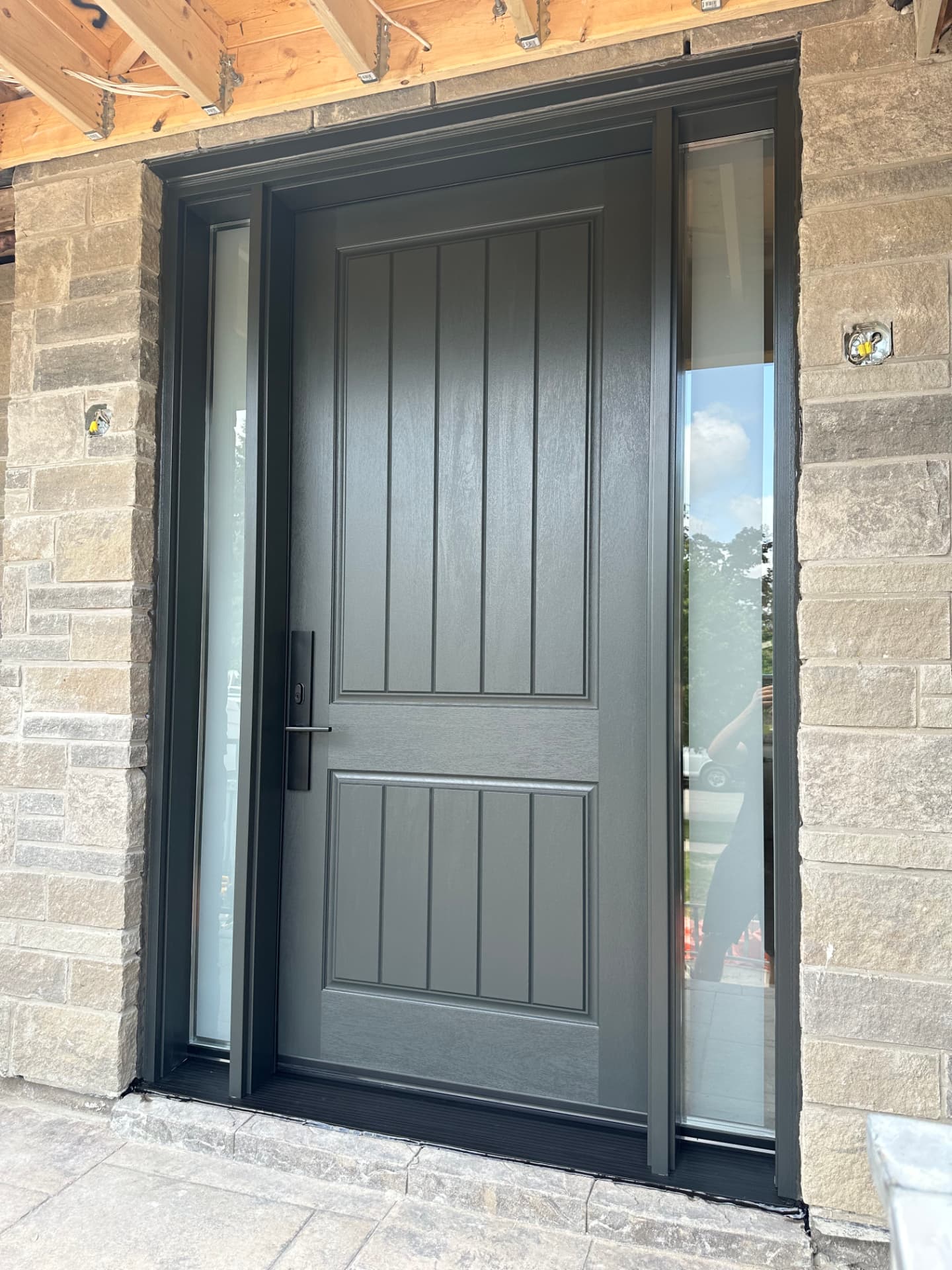 Single black plank-style entry door with two glass sidelites in the same stone porch