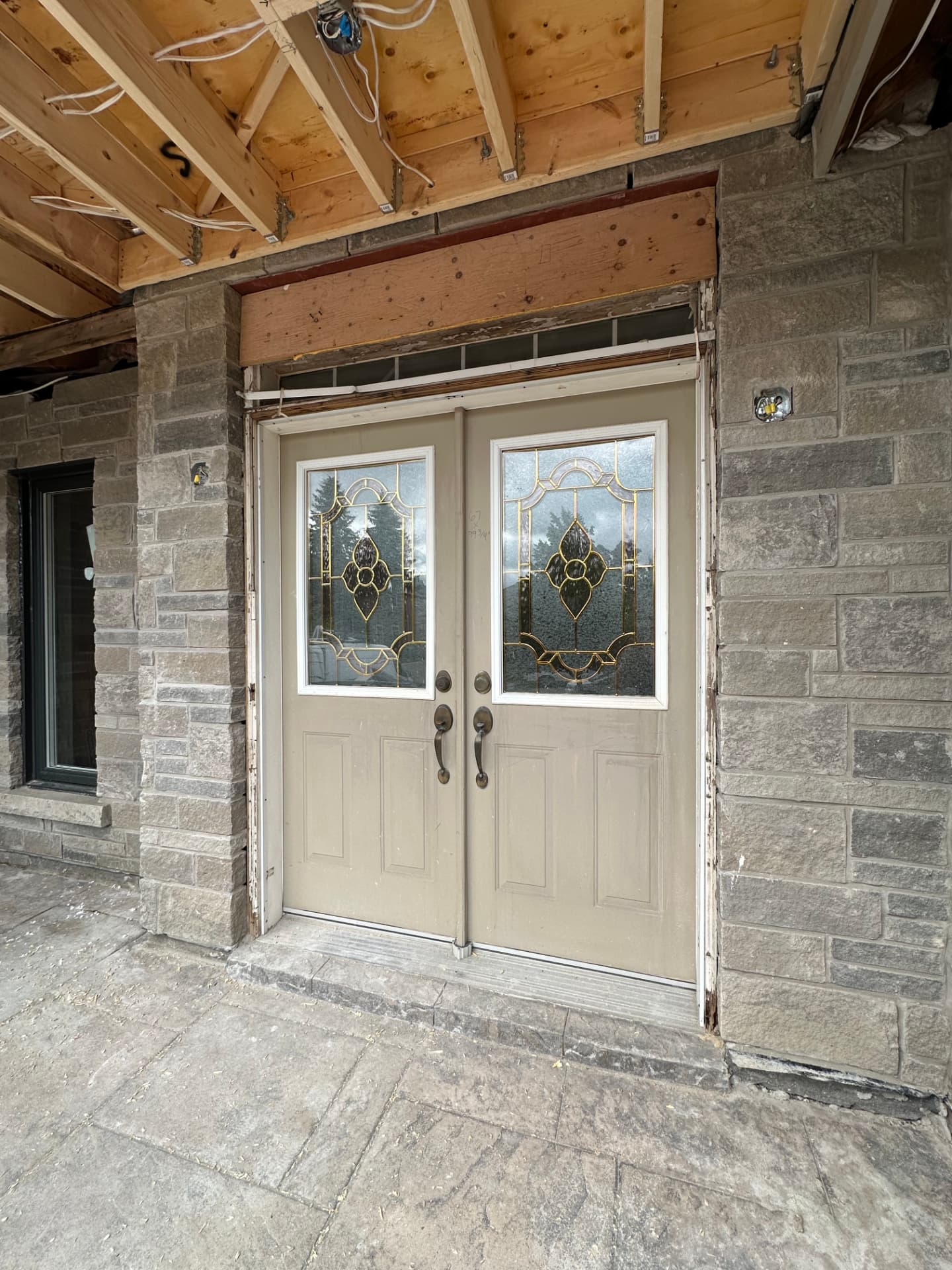 Beige double entry doors with decorative leaded glass in a stone porch under exposed framing